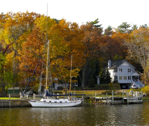 Sailboat moored along the Kalamazoo River in October with leaves turning in trees on the shore